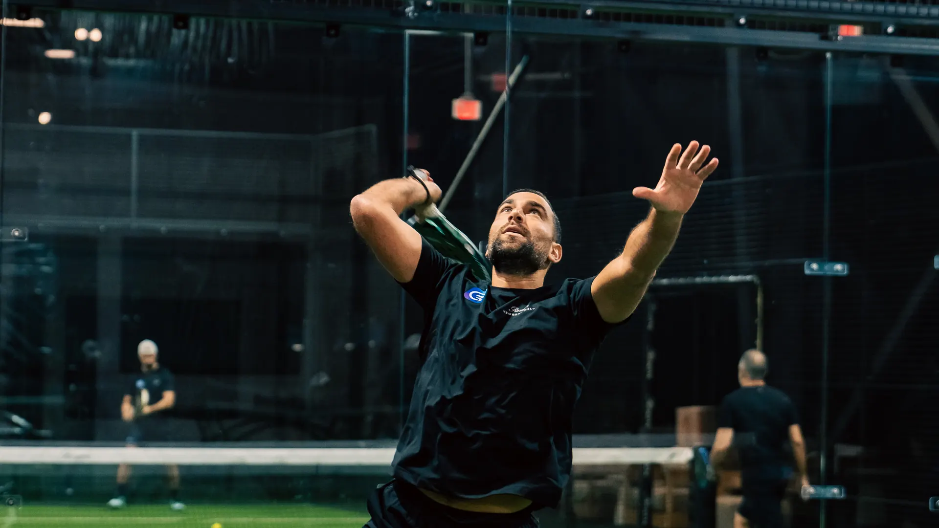 A player in a Genaya shirt leaps into an overhead smash